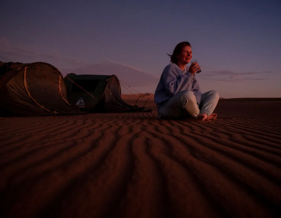 Woman sat on sand at night with tents behind her