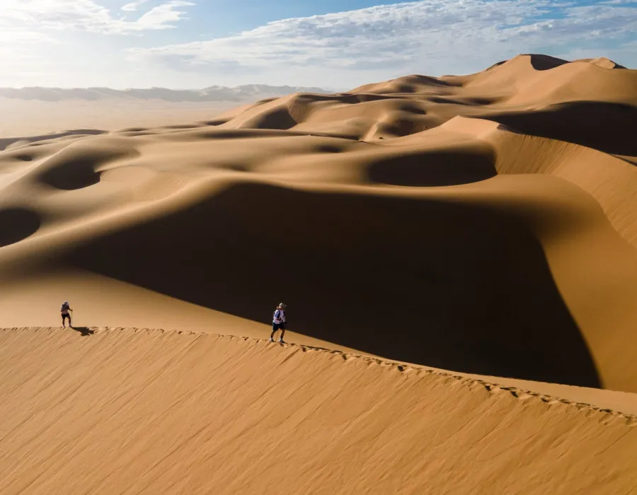 Two people walking over smooth sand dunes