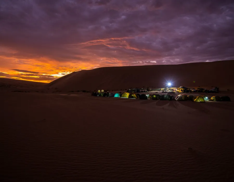 Tents next to sad dunes with dark, colourful sky behind