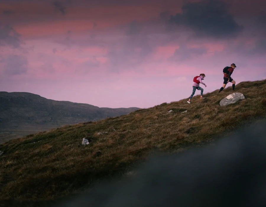People walking up grassy hill with colourful sky behind