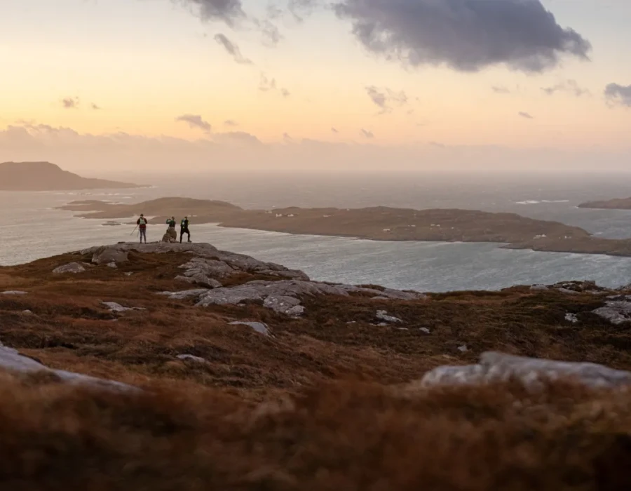 People stood on rocky coast with colourful sky above