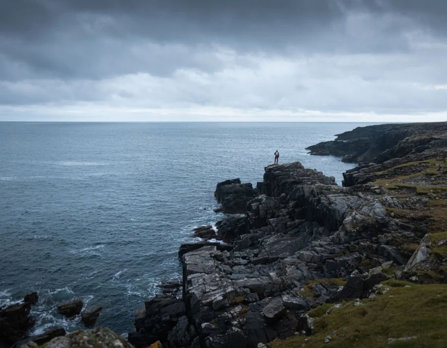 Person stood on rocks, looking out to sea