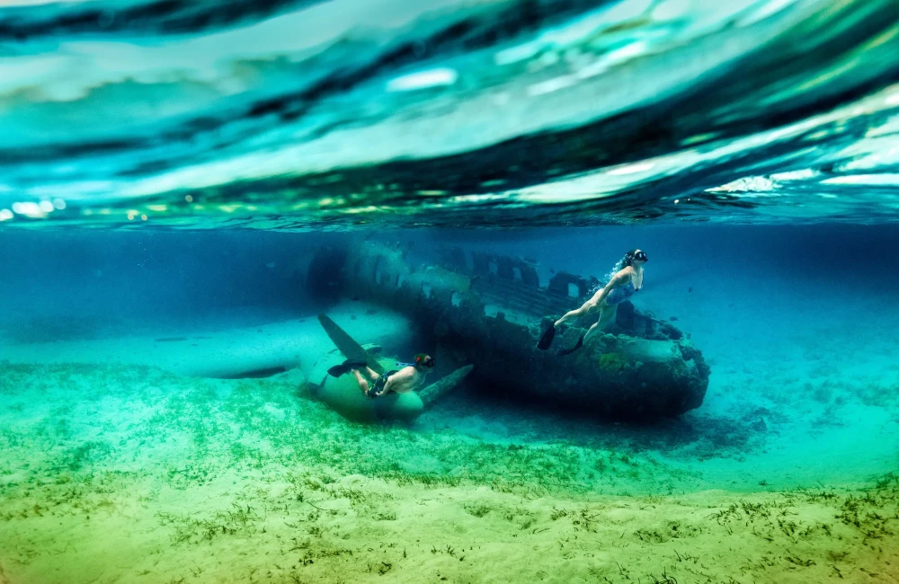 Man and woman snorkelling next to a plane wreck in clear water