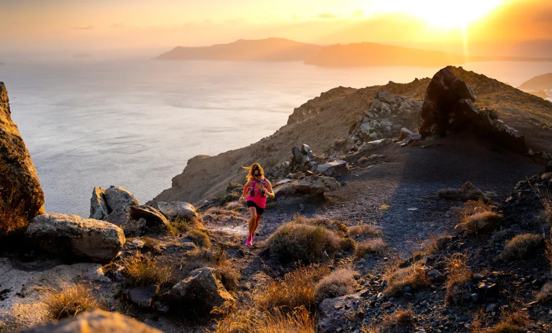 Woman running up rocky terrain with sunset behind her