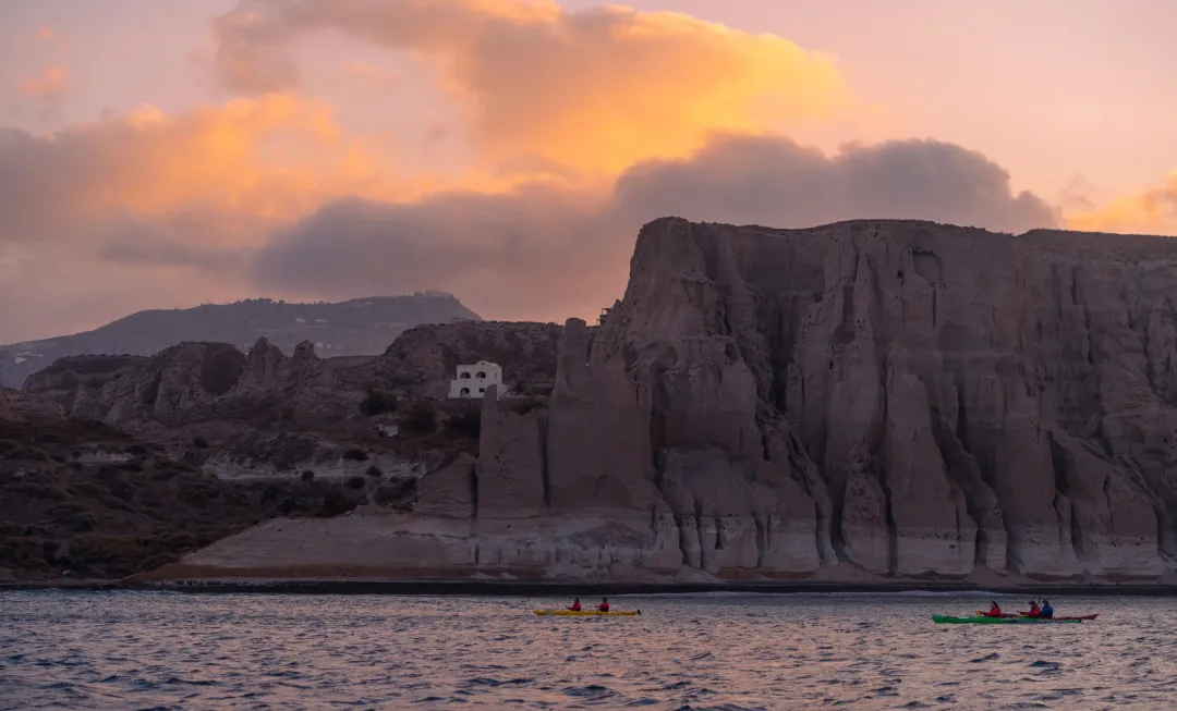 Participants kayaking through sea at sunset