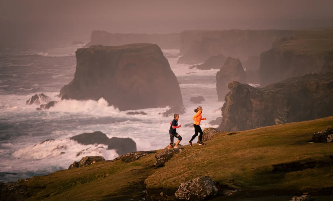 Women running up hill with cliffs and sea behind them