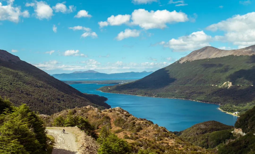 Cyclist riding along rocky path next to water and mountains