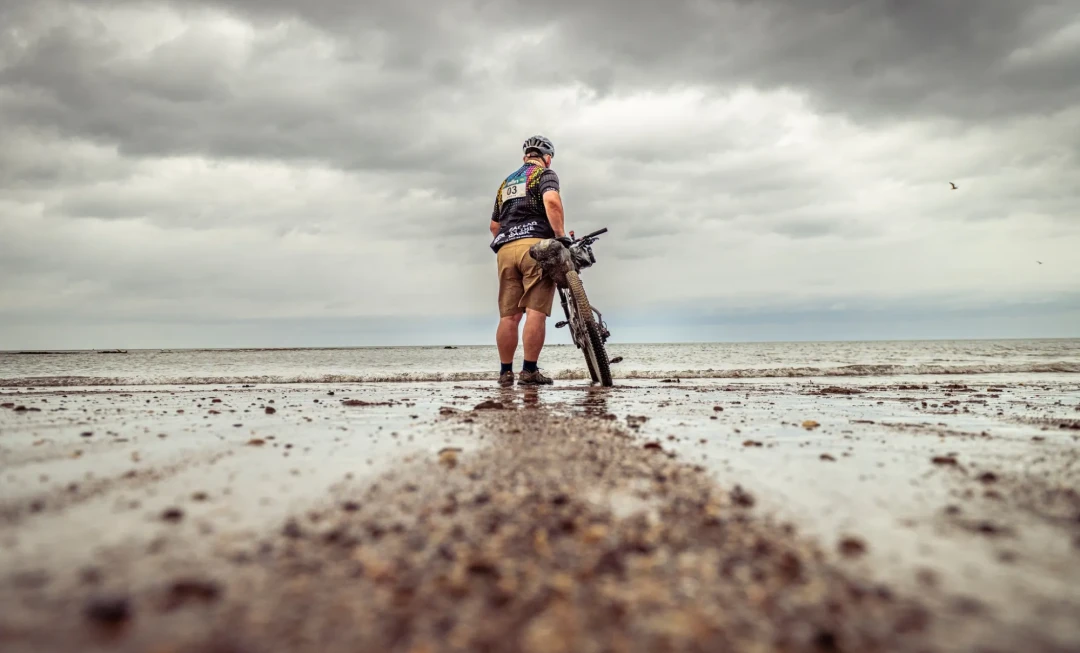 Man walking on wet sand with bike