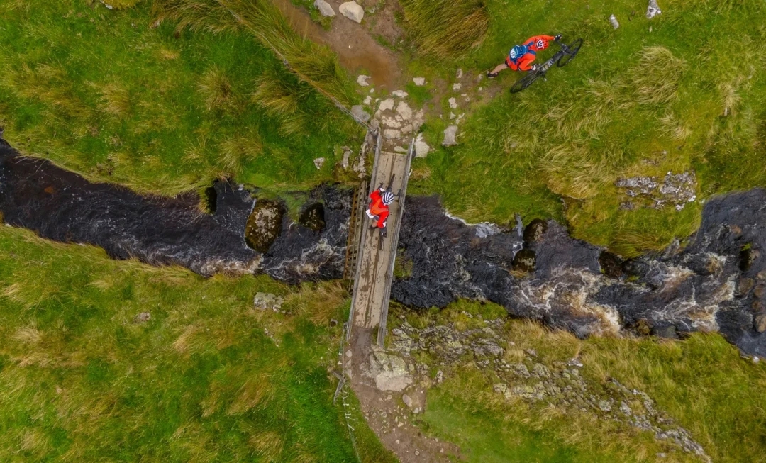 Aerial view of cyclists crossing bridge over running water