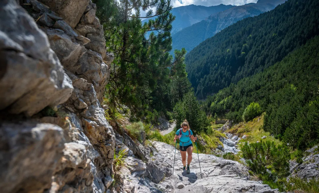 Woman hiking up rocky terrain with forests behind her
