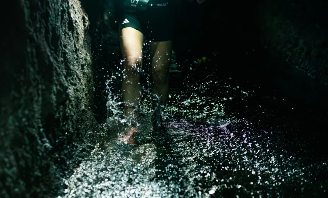 Participant holding a torch and walking through dark tunnel with shallow water