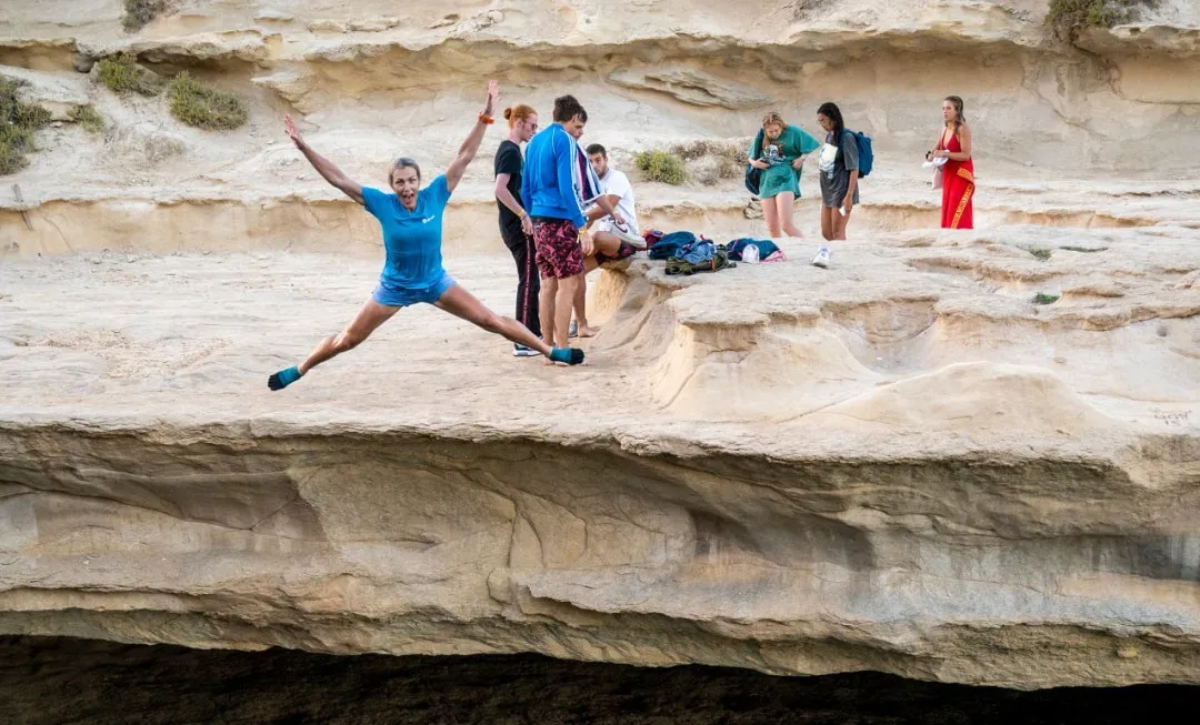 Group of participants stand on rock as woman jumps into water