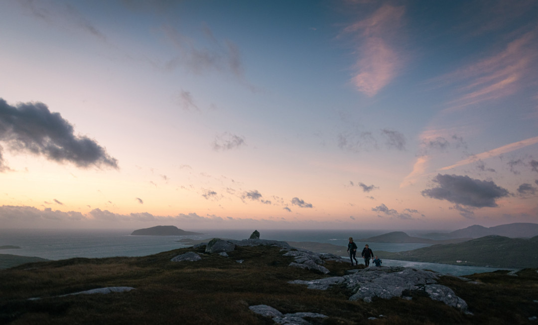 Participants running over grass and rocks with colourful sky above them