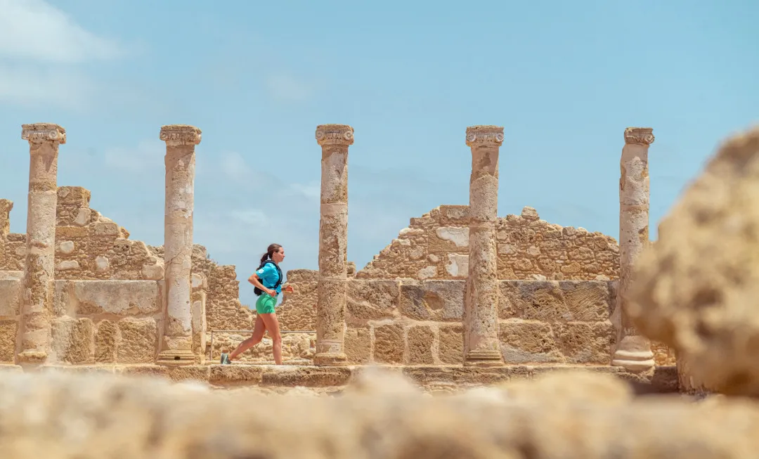 A participant runs through ancient stone ruins lined with tall columns beneath a bright blue sky