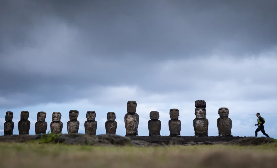Event participants running along a line of statues, with a grey, cloudy sky above