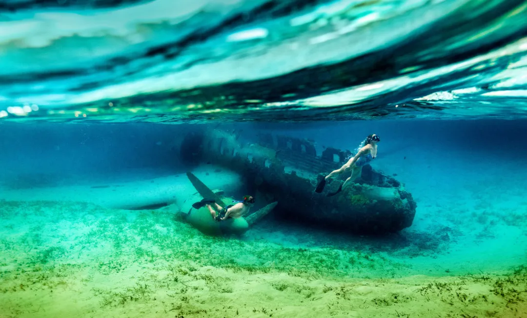 Man and woman snorkelling next to a plane wreck in clear water