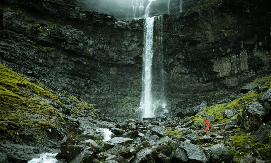 Waterfall falling from a high ledge into rocks below with splashes of greenery