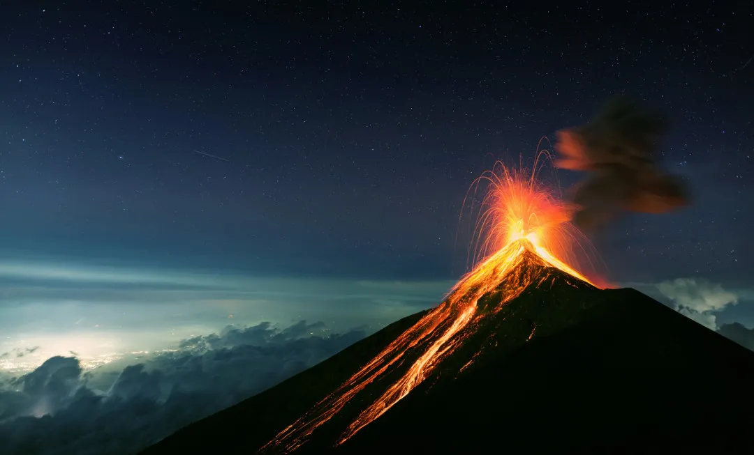 Volcano erupting with bright lava as a still, starry sky lies above