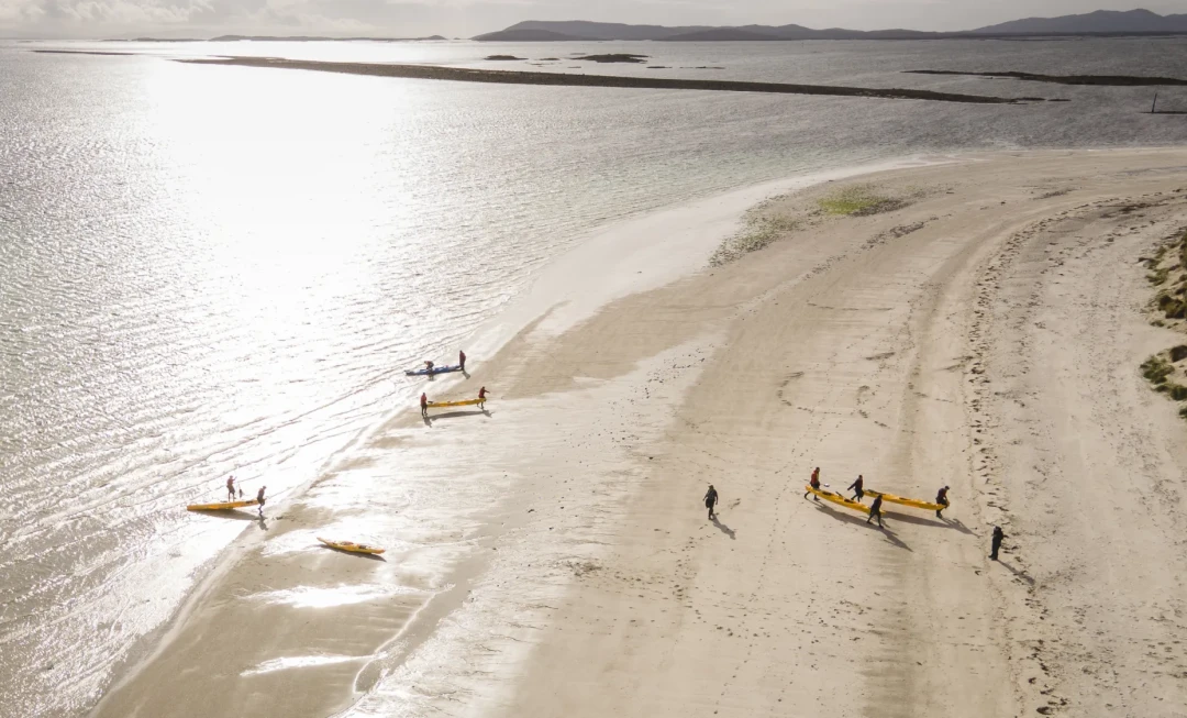 Participants lifting kayaks from water and placing them on sandy beach