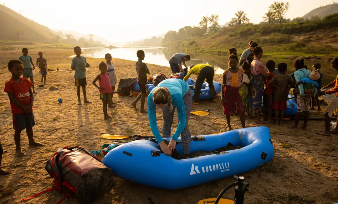 Participants setting up rafts by river and surrounded by local children