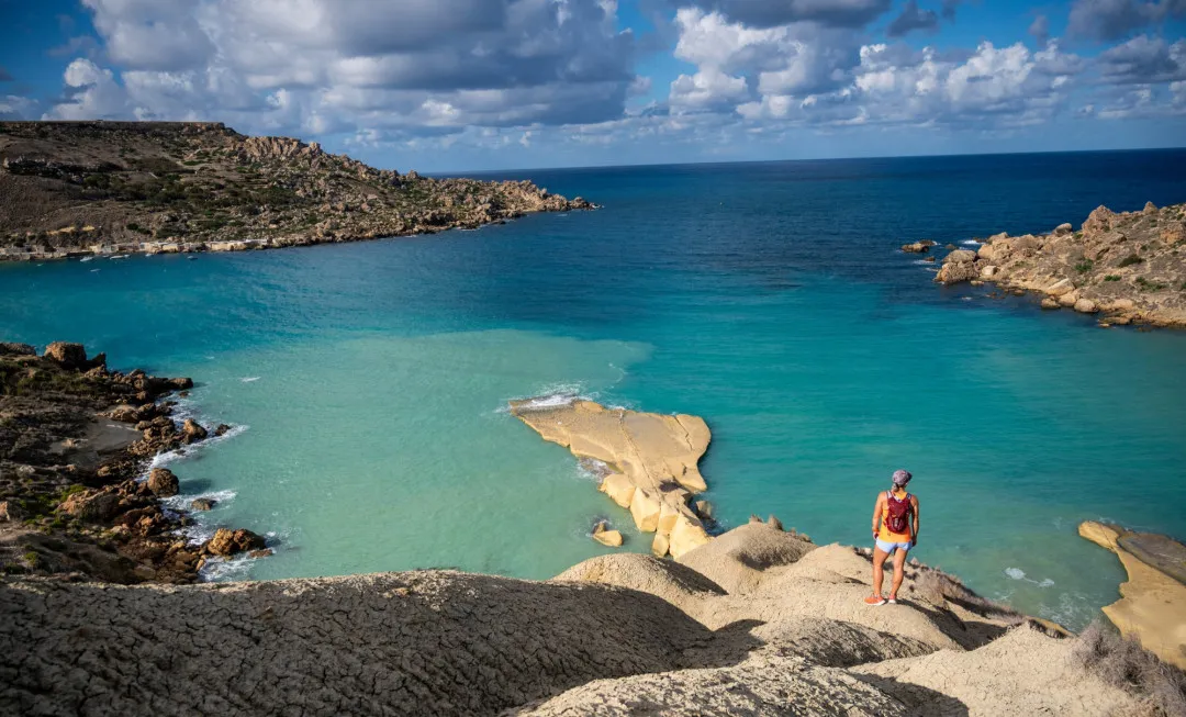 Woman stood on rocks, looking out to clear, still sea