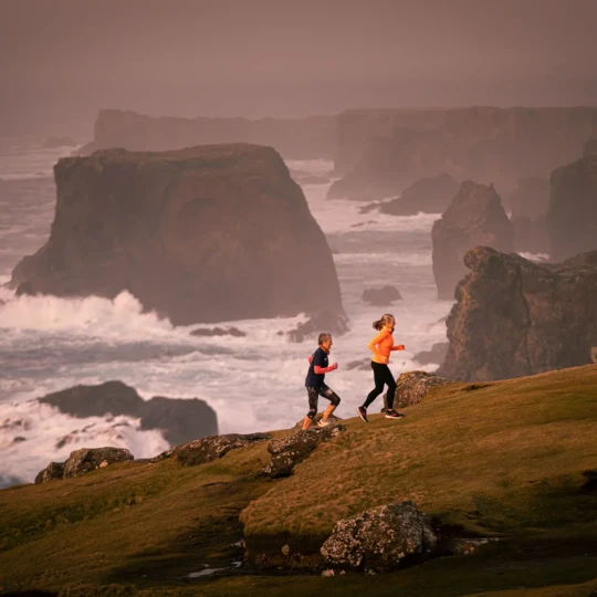 Women running up hill with cliffs and sea behind them