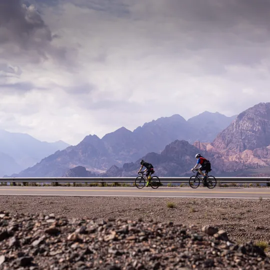 Cyclists riding along road with mountains in background