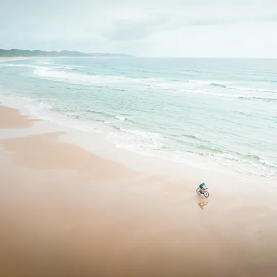 Woman cycling along sandy coastline