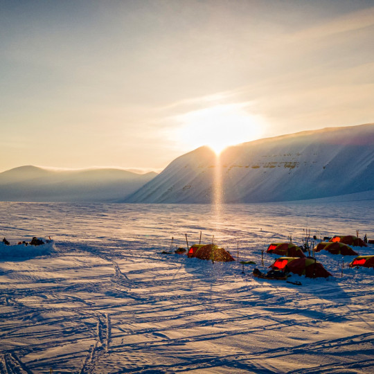 Tents pitched in deep snow with low sign behind a mountain