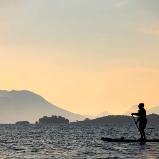 A lone event participant paddleboards across calm water, with a pink sky and hills in the background