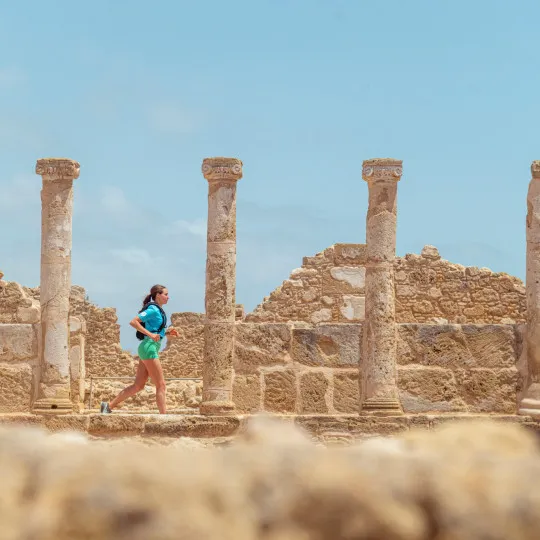 A participant runs through ancient stone ruins lined with tall columns beneath a bright blue sky