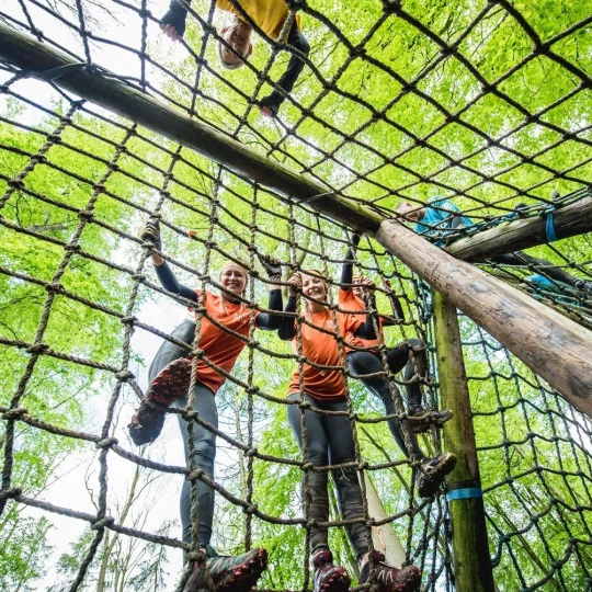 Smiling participants climbing up a rope obstacle in a forest