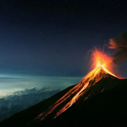 Volcano erupting with bright lava as a still, starry sky lies above