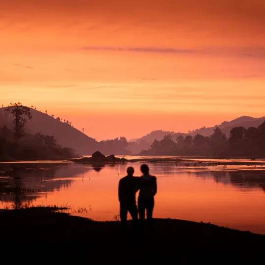 Silhouettes of two participants with their arms around one another with colourful sky above