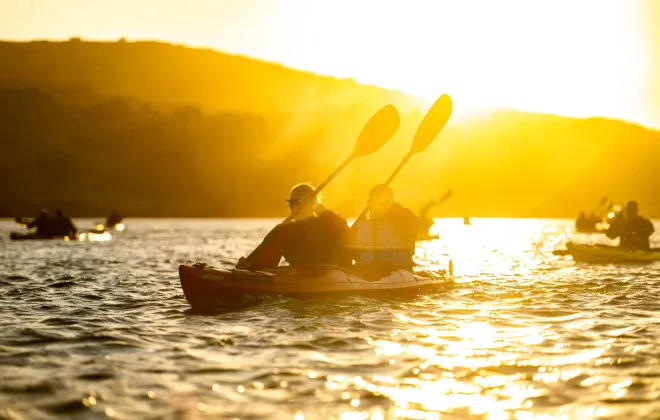 Participants kayaking with bright, low sun