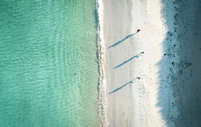 People running along sandy beach next to clear water