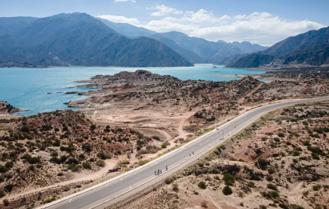 Cyclists riding along road with water and mountains behind