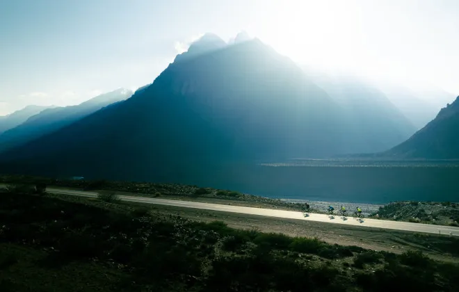 Cyclists riding along road past mountains