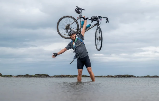 Man stood in water and holding his bike above his head