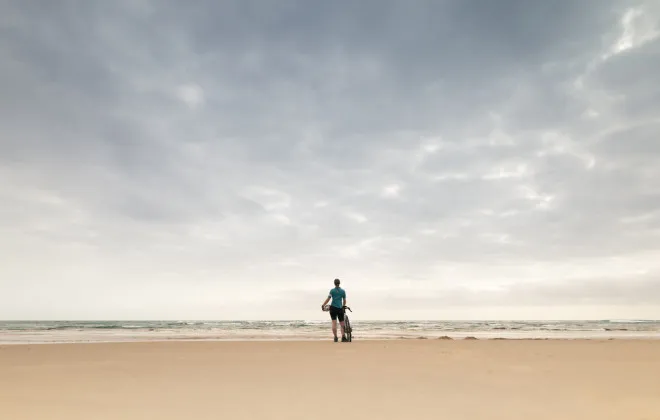 Woman standing on sandy beach with bike