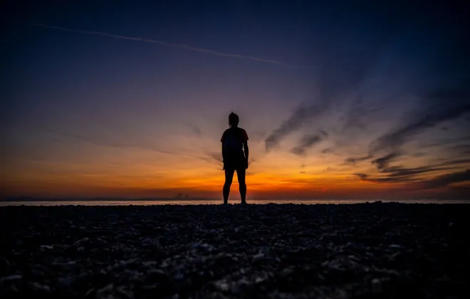 Woman stood looking out to sea and colourful sunset above