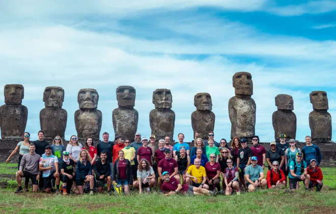 Group of smiling participants in colourful clothes with statues behind them and a blue sky above