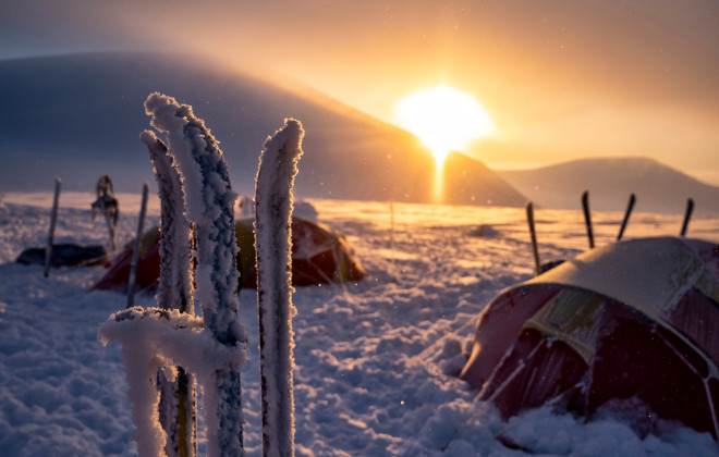 Snow-covered tents and a low, colourful sun behind
