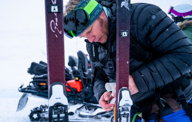 Man fixing skis in a snowy, white environment