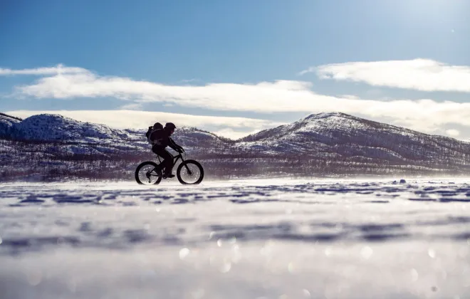 Single cyclist riding across a snowy landscape on a fat bike