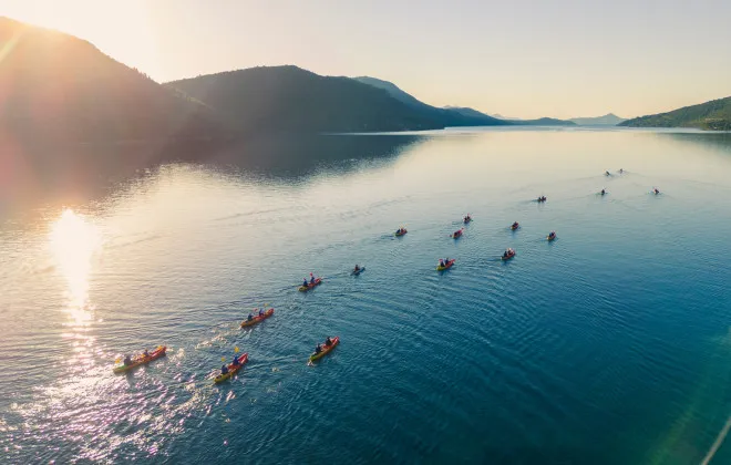 Group of participants kayaking across sunlit open water with mountains either side