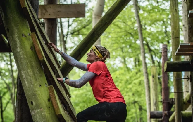 Woman climbing up a wooden ladder as part of an obstacle course in a forest