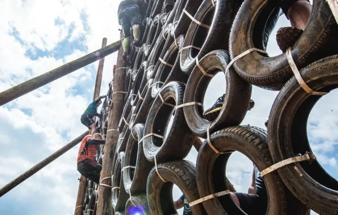 Participants climbing up a muddy wall of tyres