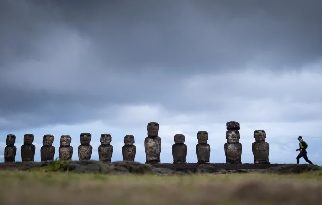 Event participants running along a line of statues, with a grey, cloudy sky above