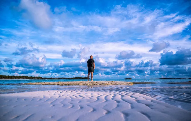 Man stood on a sandy beach looking out to the sea
